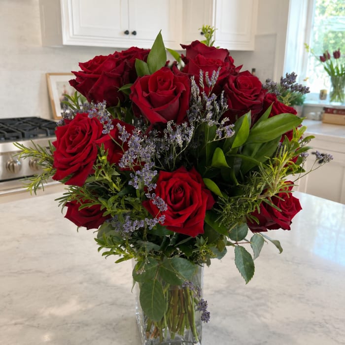 Red roses arranged in a clear glass vase with purple filler flowers.