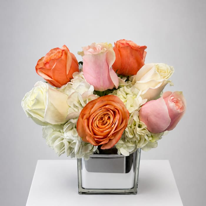 Bouquet of orange, pink, and white roses in a square glass vase