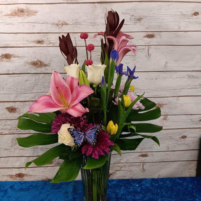 Mixed bouquet in a tall glass vase with pink lilies, roses, and blue flowers