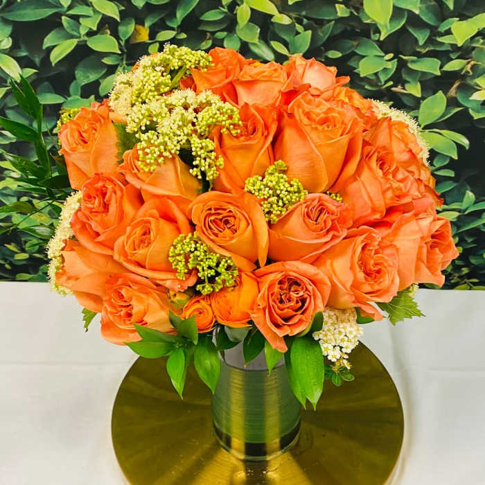 Orange roses arranged in a gold vase on a round gold base