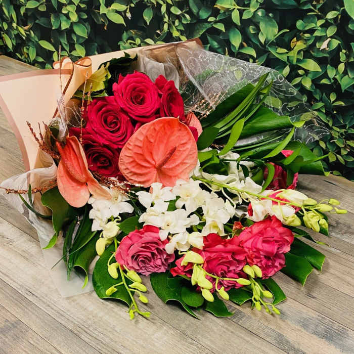 Bouquet of red roses, pink anthuriums, and white orchids with green leaves
