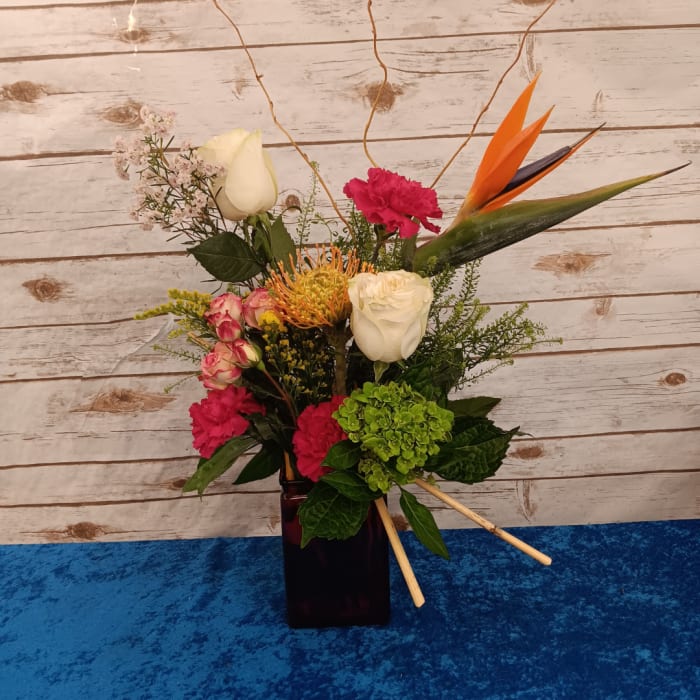 Mixed floral arrangement in a dark rectangular vase with white roses and bright tropical blooms