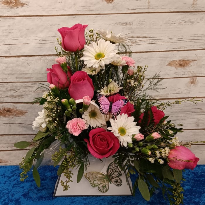 Pink roses and white daisies arranged in a decorative box with a butterfly accent.
