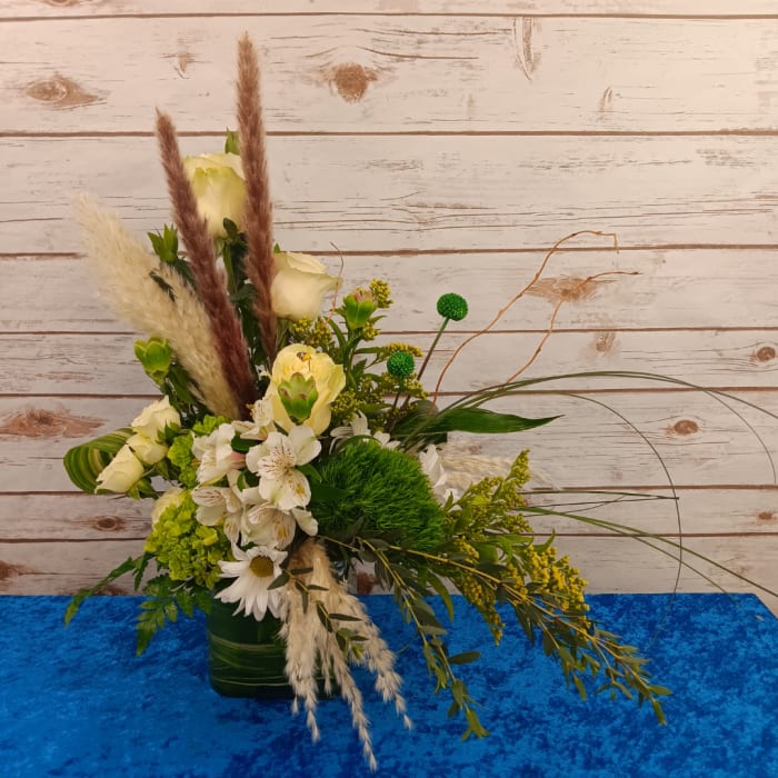 Mixed floral arrangement in a green vase with white blooms and tall dried grasses
