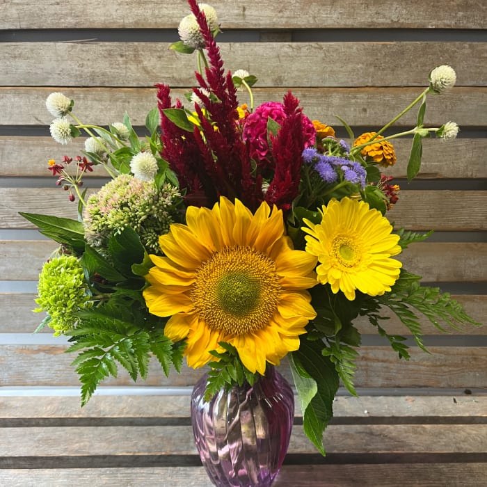 Mixed bouquet with sunflowers, yellow daisies, and a purple vase