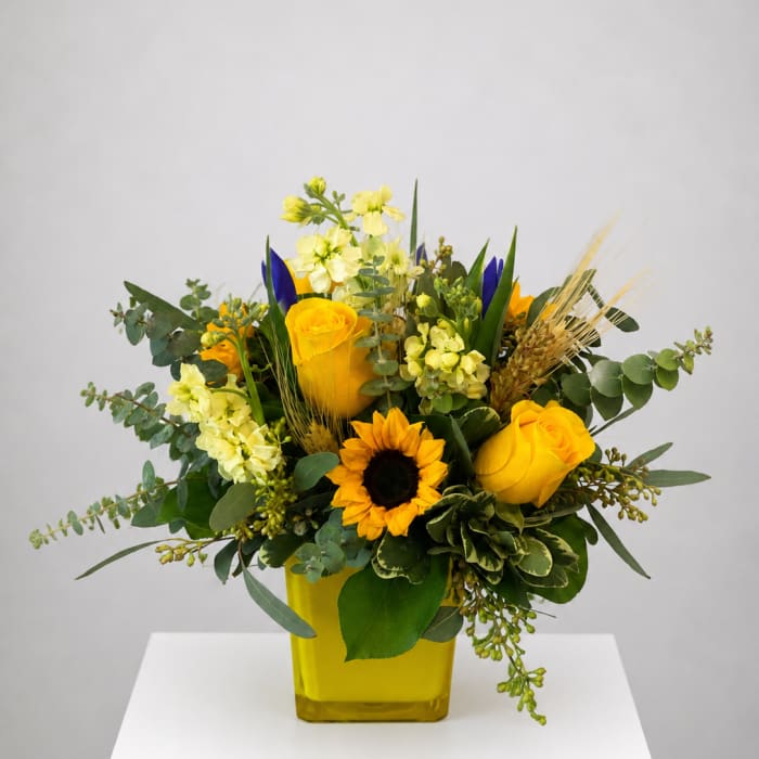 Yellow roses and a sunflower in a yellow vase with mixed greenery