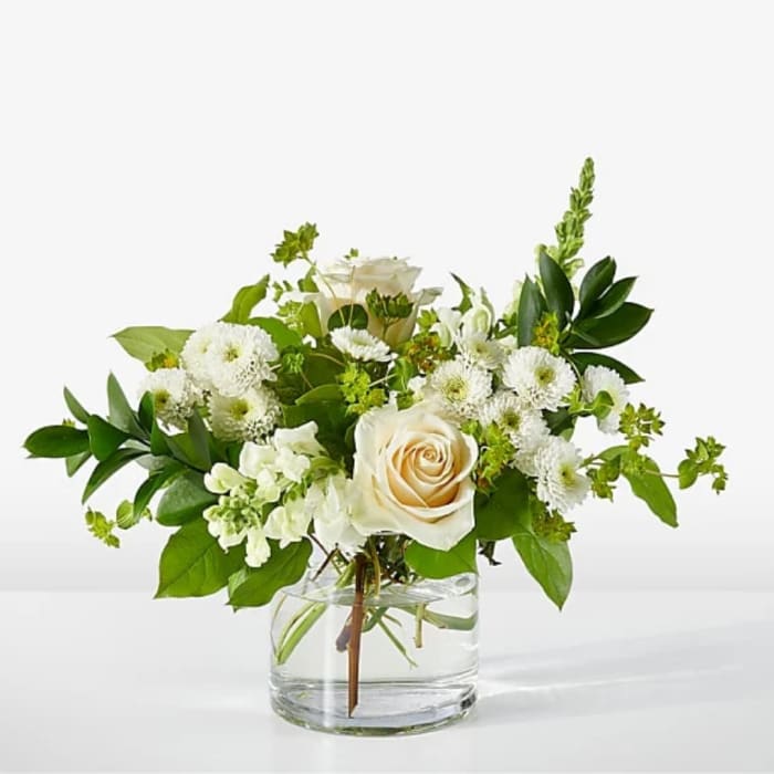 White roses and daisy-like blooms in a clear glass vase