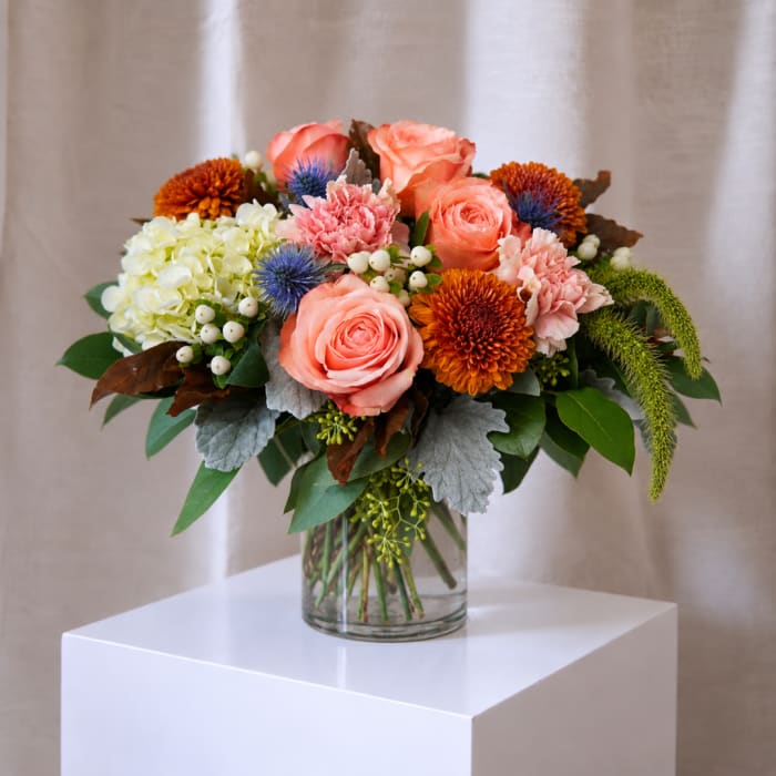 Mixed bouquet of peach roses, hydrangea, and mums in a glass vase