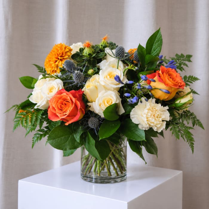 Mixed bouquet of roses, carnations, and blue thistle in a glass vase