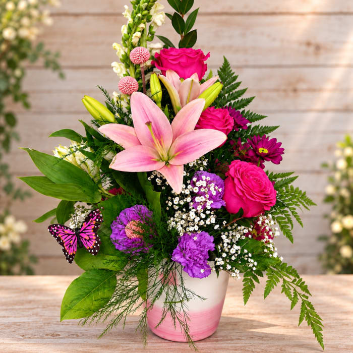 Pink lilies and roses in a white-and-pink vase with a butterfly accent