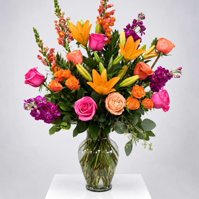 Bright mixed bouquet with roses, lilies, and purple blooms in a glass vase