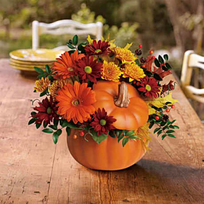 Pumpkin centerpiece with orange and red flowers on a wooden table