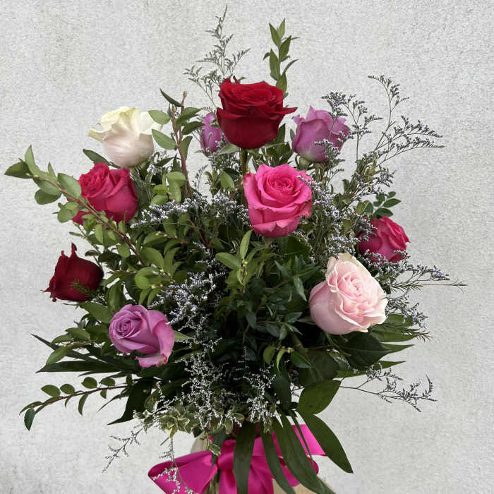 Tall mixed arrangement of red, pink, and lavender roses in a glass vase with a pink bow