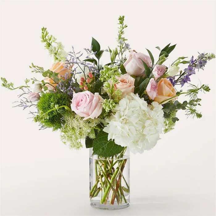 Mixed bouquet of pink and peach roses, white hydrangea, and accents in a clear glass vase