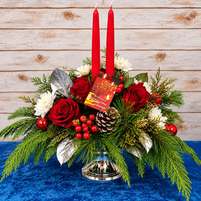 Holiday centerpiece with red candles, roses, and white daisies in a silver vase