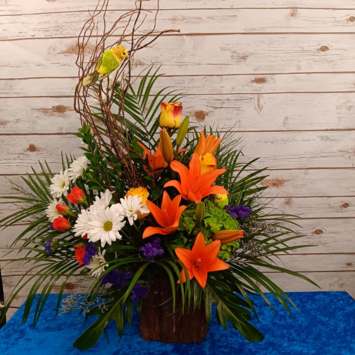 Tropical floral arrangement with orange lilies, white daisies, and a decorative bird