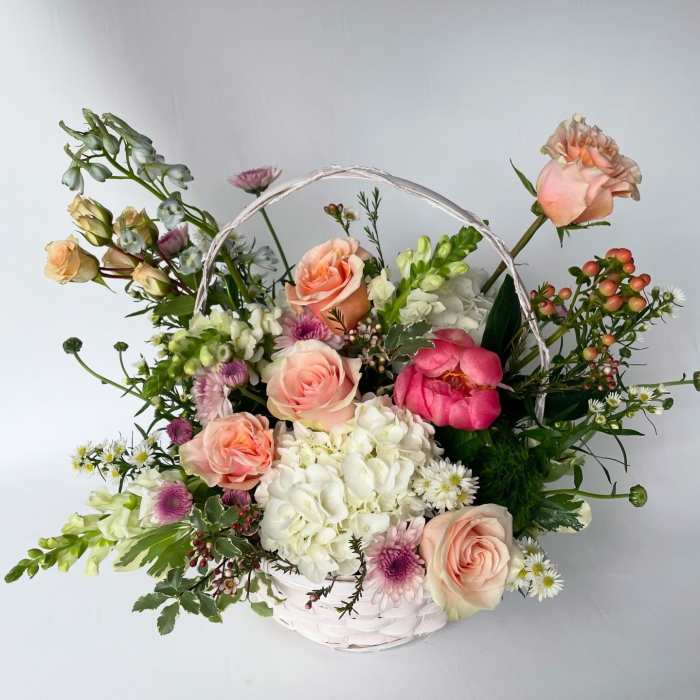 Basket arrangement of peach roses, white hydrangea, and mixed blooms