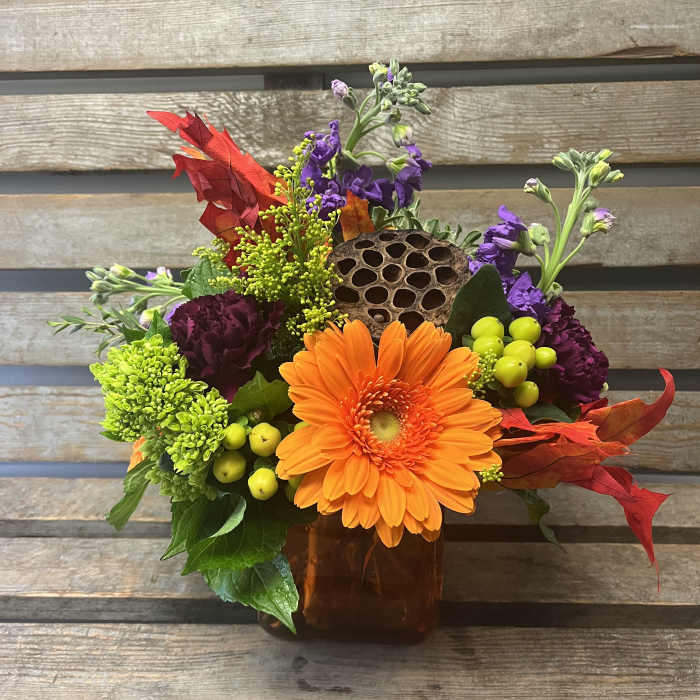 Orange gerbera bouquet in a square vase with purple and green accents