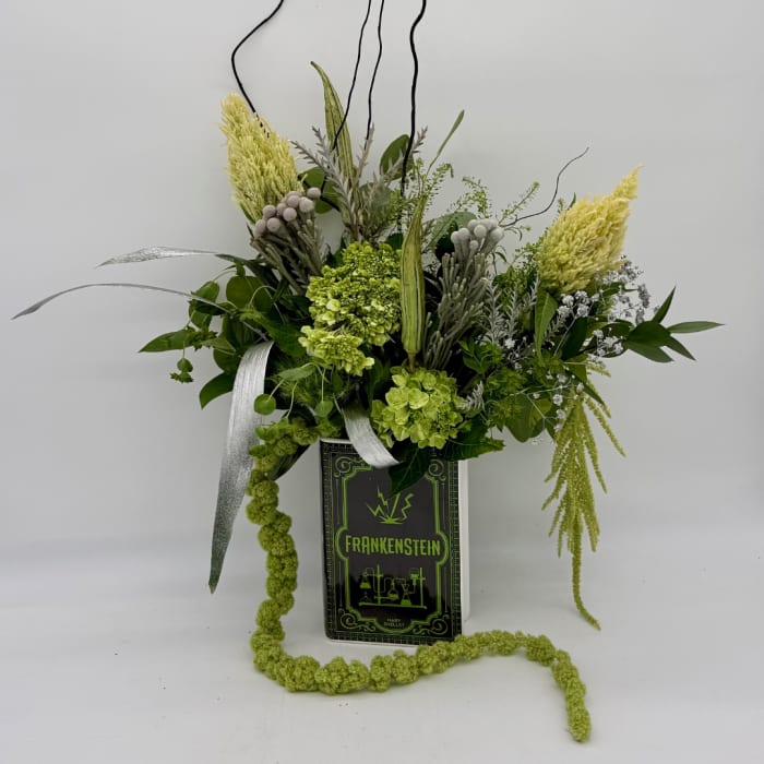 Green floral arrangement in a Frankenstein book-shaped container