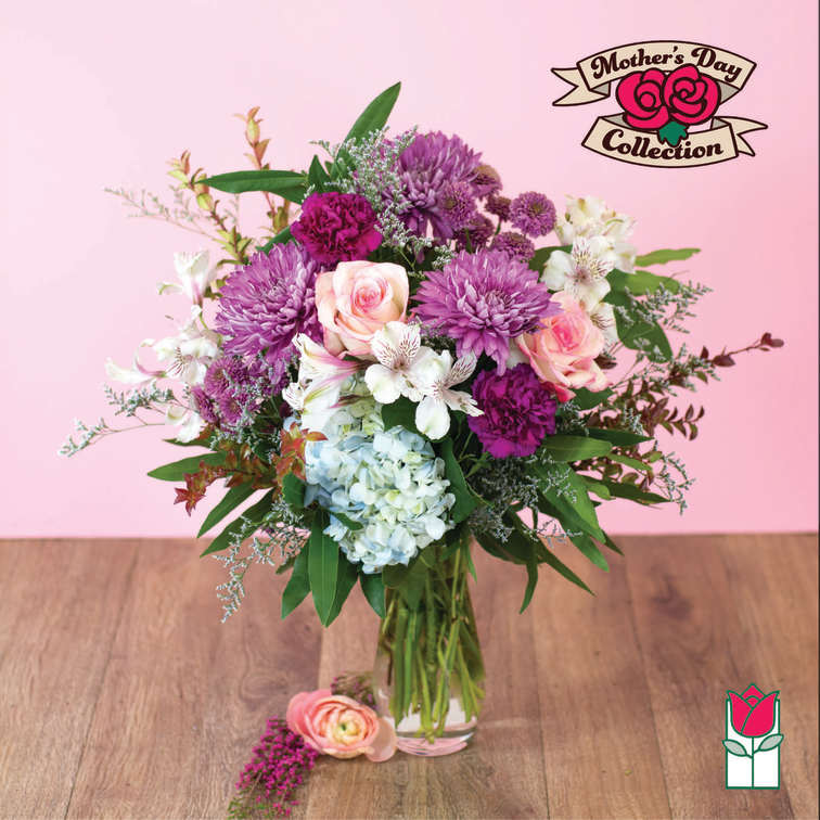 Mixed bouquet of purple mums, pink roses, and blue hydrangea in a clear glass vase