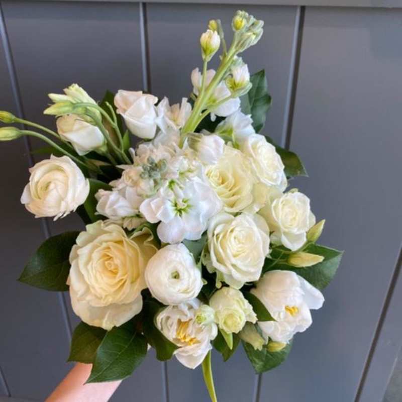 Hand-held bouquet of white roses and other white blooms against a gray paneled background