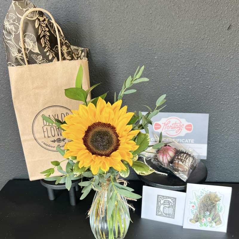 Sunflower arrangement in a glass vase with a gift bag and chocolates