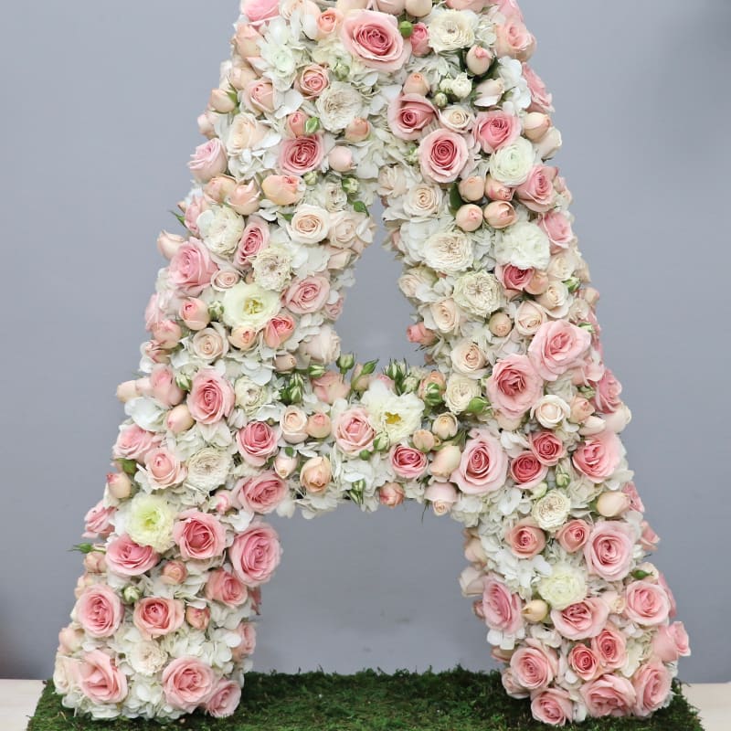 Tall floral letter A made of soft pink and white roses and hydrangeas on a moss-covered base