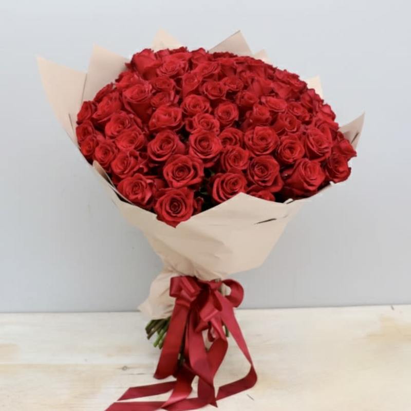 Large bouquet of red roses wrapped in beige paper with a red ribbon bow