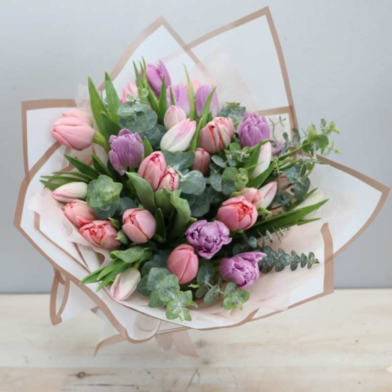 Hand-tied bouquet of pink and purple tulips with eucalyptus wrapped in white and beige paper.