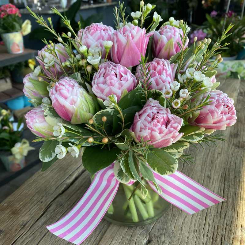 Pink tulip bouquet in a glass vase with a striped ribbon