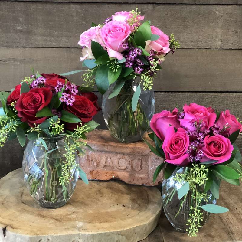Three rose bouquets in glass vases on wooden stands