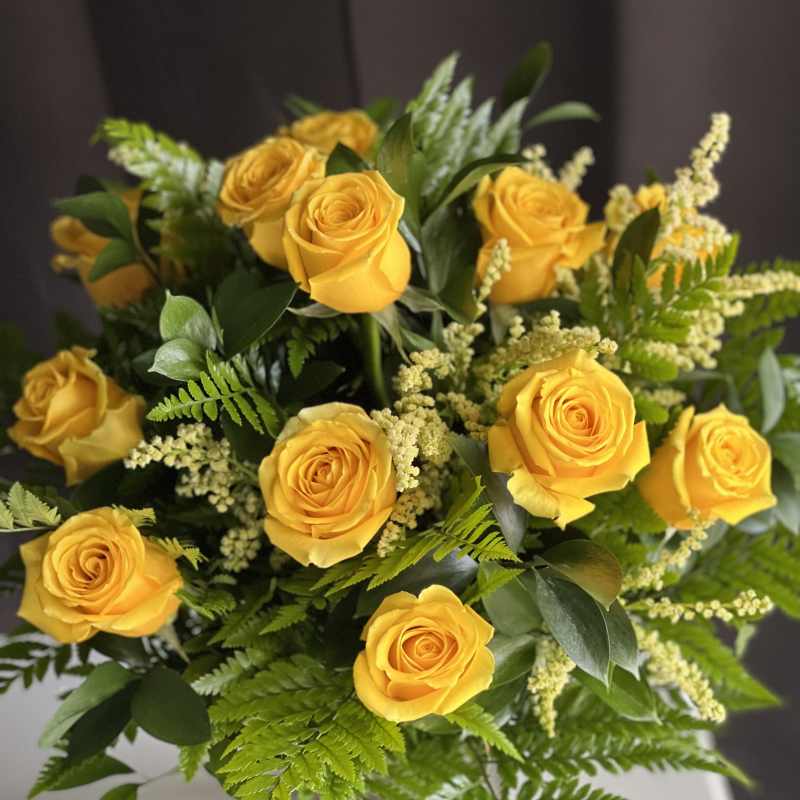 Bouquet of yellow roses with green foliage in a clear vase