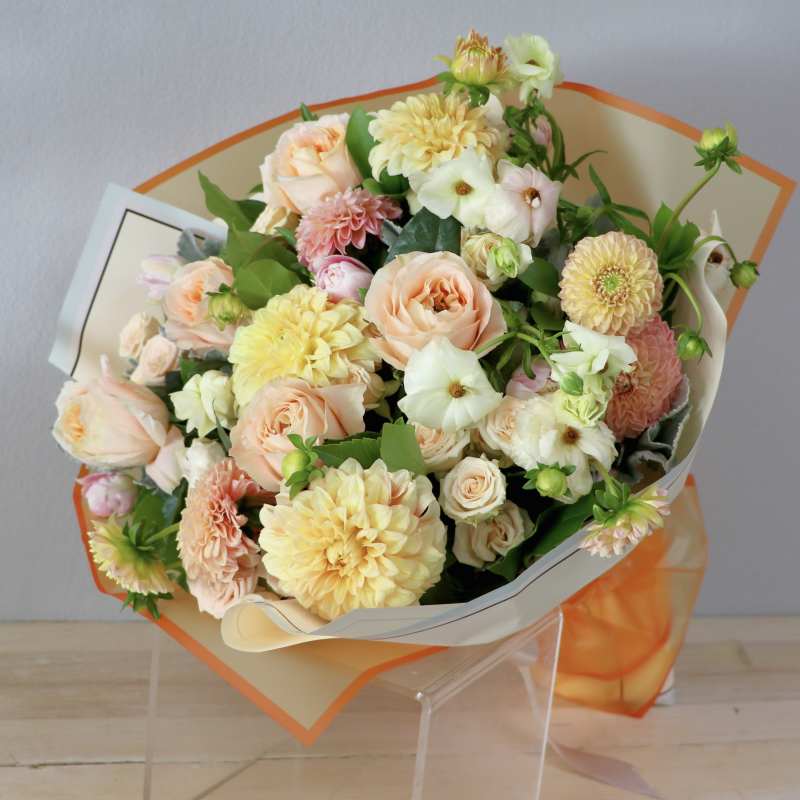 Bouquet of peach roses and pale yellow dahlias wrapped in cream and orange paper