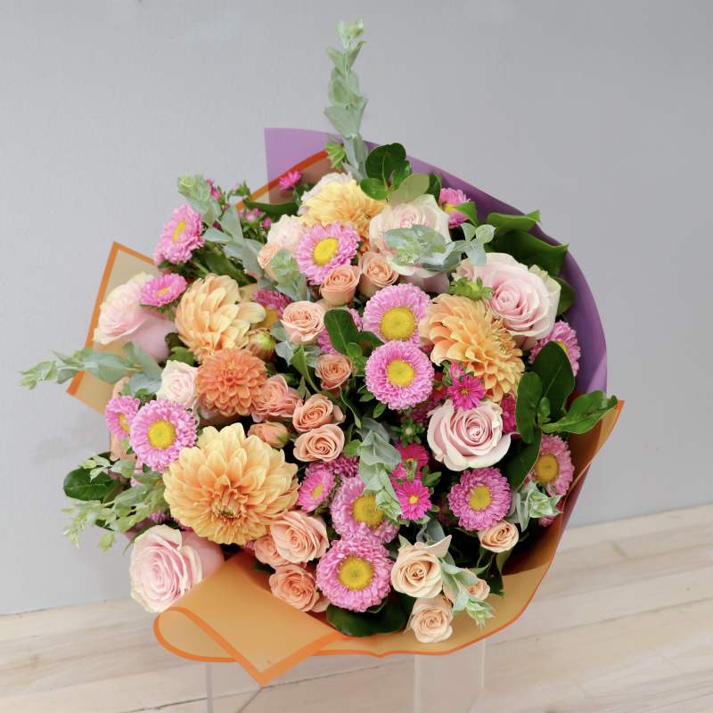 Bouquet of pink and peach flowers wrapped in orange and purple paper