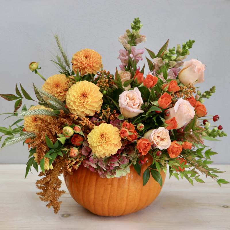 Autumn arrangement of orange and peach flowers in a hollow pumpkin container