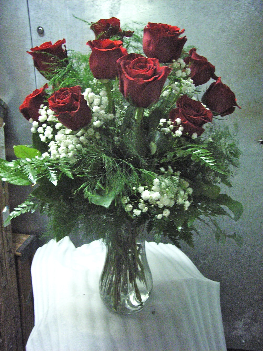 One dozen velvety deep red roses arranged in a vase with greenery