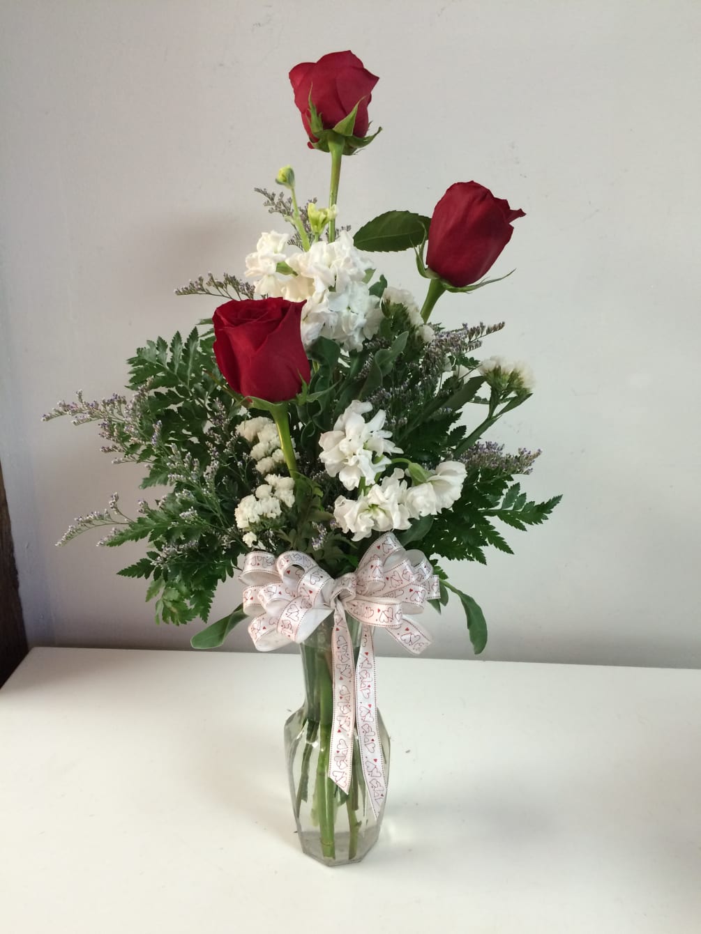 3 roses with accent flowers in a clear glass vase.  Includes