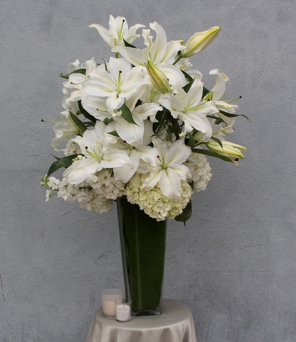 Lilies, hydrangeas, stock and greens in a tall glass vase. 