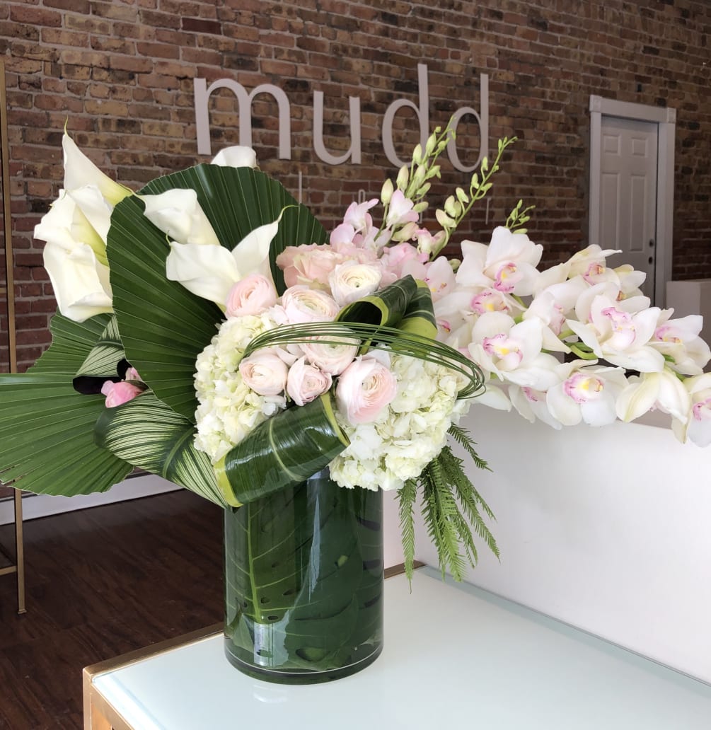 An extravagant arrangement of premium blush and cream flowers with tropical foliage