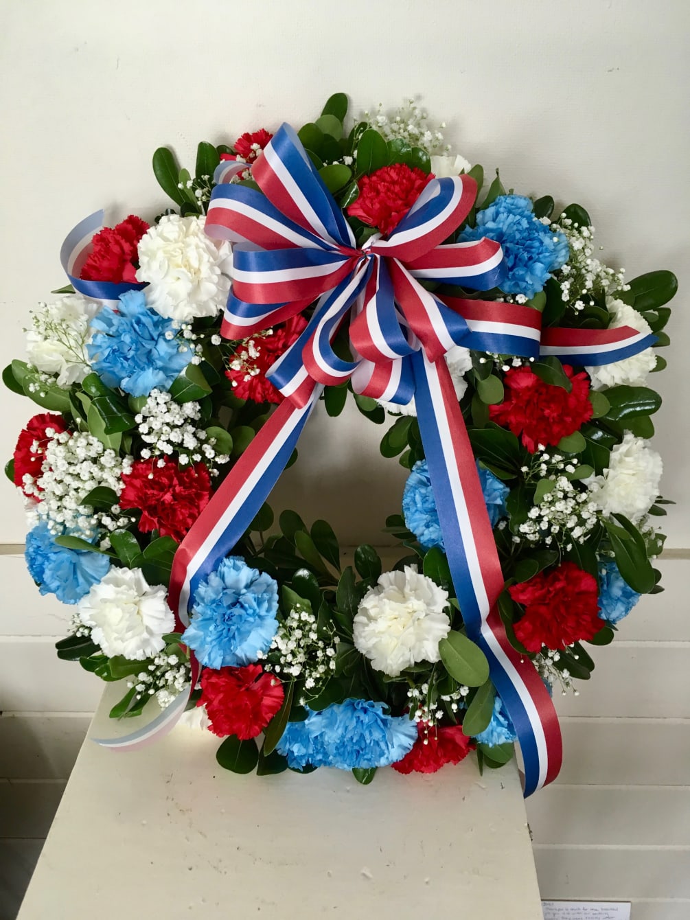 18 inch round wreath with greenery boasting red, white and blue carnations