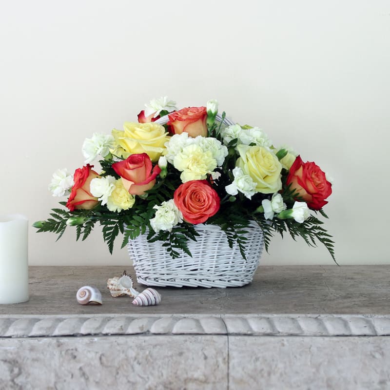 A mingling of carnations and roses crafted in a white willow basket