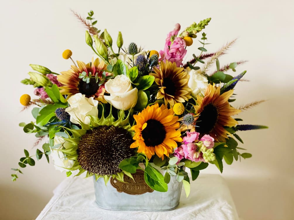 A beautiful display of seasonal sunflowers, roses, snapdragons, grasses and thistle to