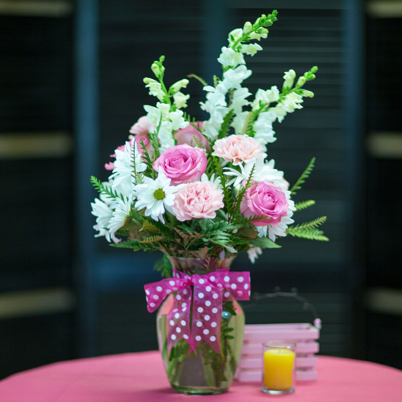A splash of pink roses and pink carnations accent the white snapdragons