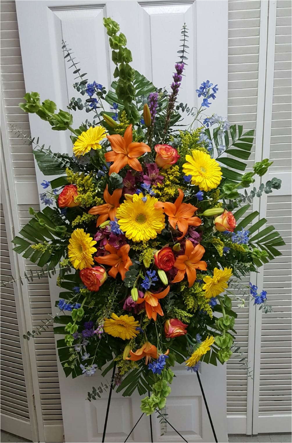 This Sympathy Easel consists of Green Bells of Ireland, Blue Delphinium, Yellow