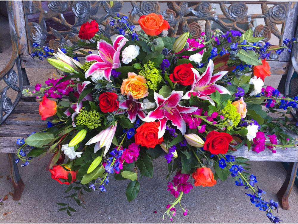 Beautiful, brightly colored casket spray with stargazer lilies, orange and red roses