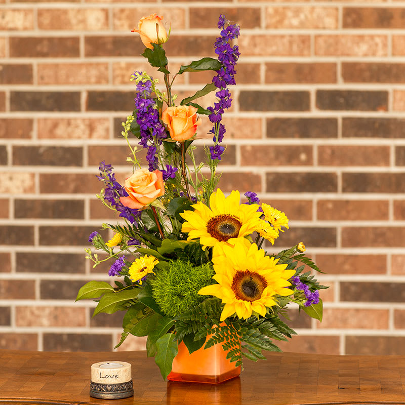 Cube vase of sunflowers, roses, larkspur, Viking pom, statice, and other.