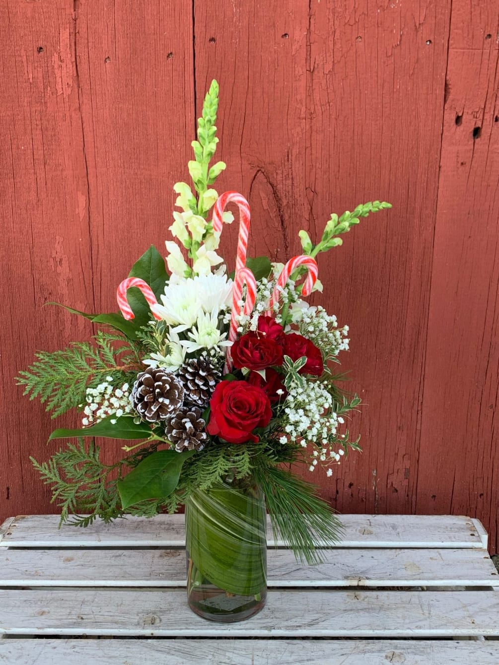 A festive arrangement including roses, pine cones, snapdragons, winter greens and other
