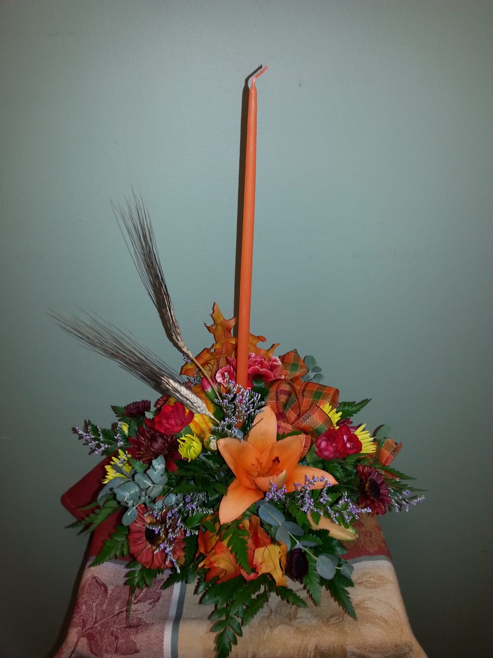 A tasteful Candle centerpiece of Lilies, Mums, Carnations and festive trim to