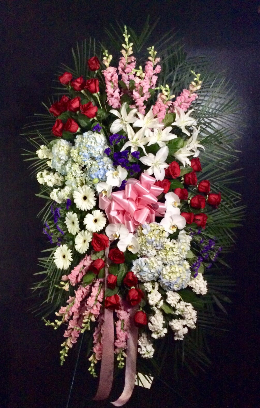 Beautiful standing spray with red roses,blue hydrangeas, pink snap dragons, white stock