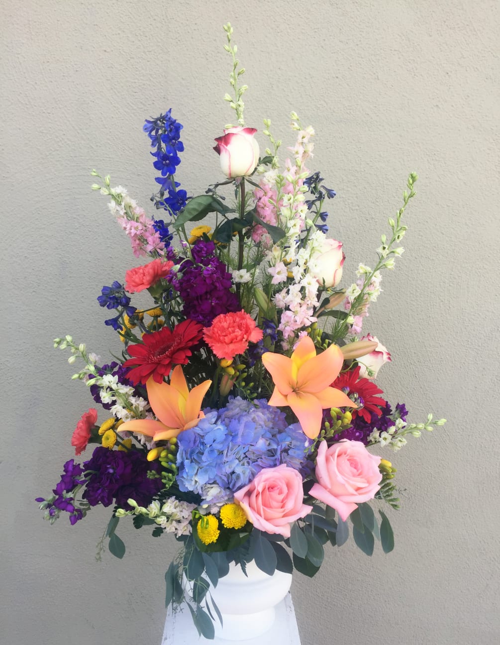 A basket arrangement with gerber daisies, larkspur, beladonna, larkspur, buttonpoms, roses, carnations